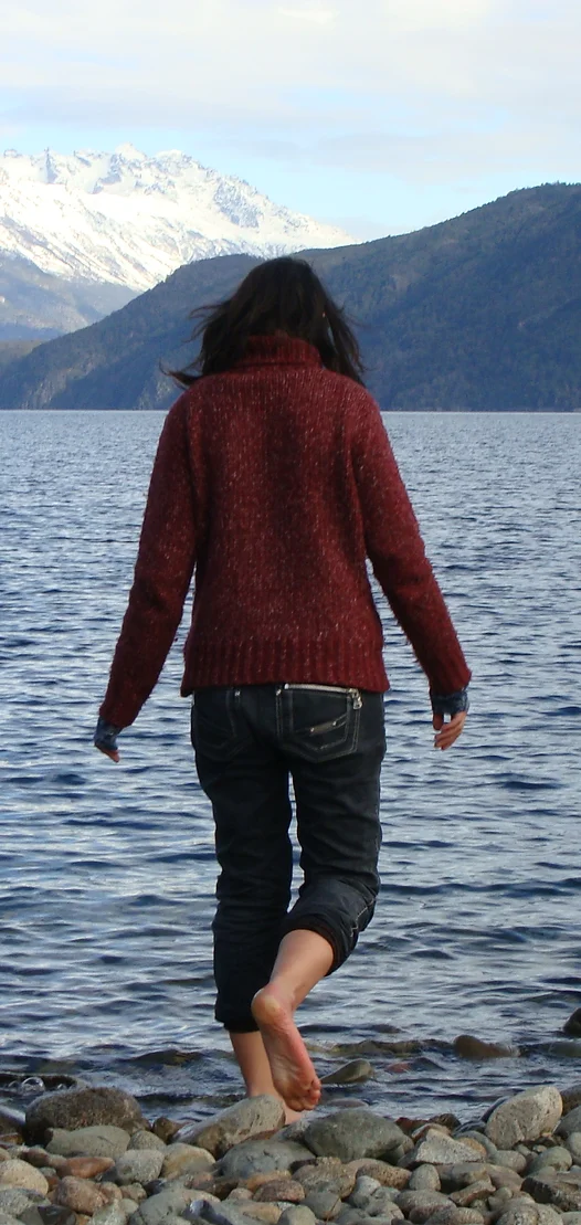 Alessia on a pebble beach with her back to the camera, facing the sea.